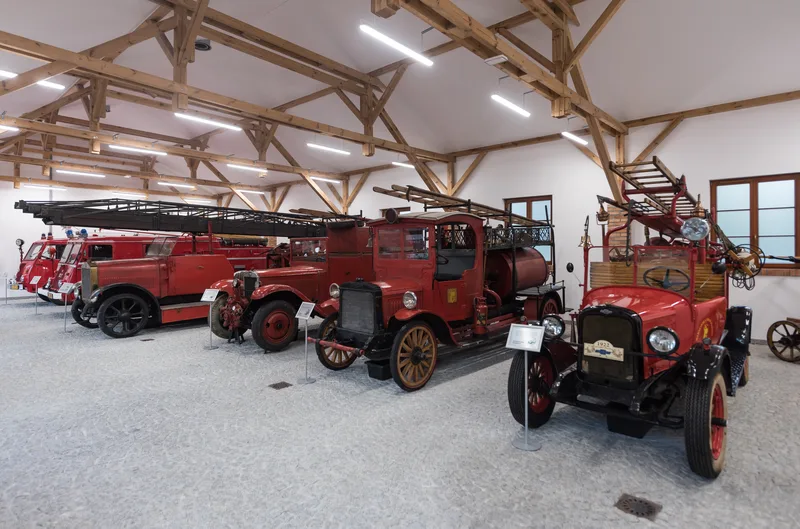 Rząd zabytkowych wozów strażackich w sali wystawowej, w tym czerwony Chevrolet z 1922 roku