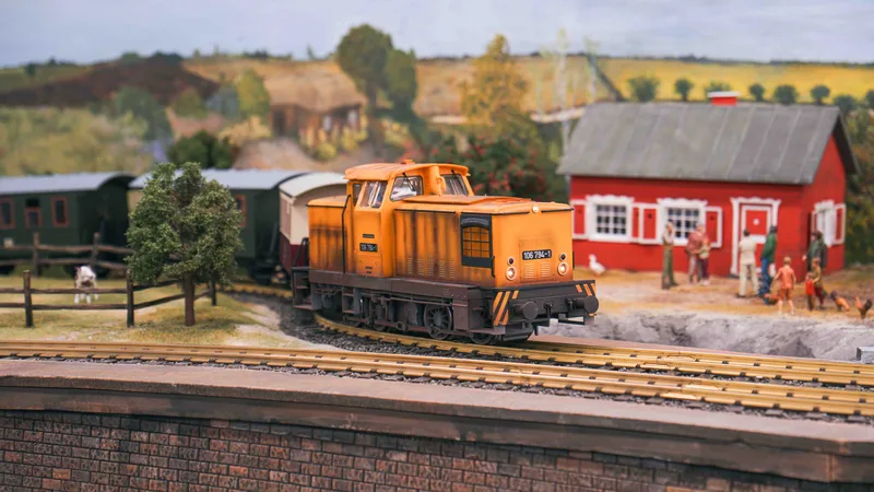 Pomaranczowa lokomotywa na makiecie Kolejkowo - wiejski krajobraz z czerwona stodola