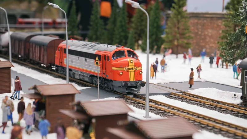 Miniaturowy pociag towarowy przejezdzajacy przez zimowy krajobraz ze sniegiem i figurkami