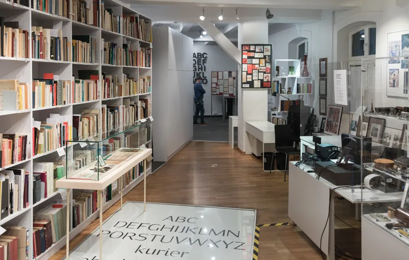 Wnętrze ekspozycji stałej „Czar czcionki” w Muzeum Drukarstwa, regały z książkami i gabloty z eksponatami typograficznymi