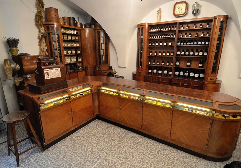 Zrekonstruowane wnętrze międzywojennej apteki w Muzeum Farmacji, z drewnianą ladą, szafami aptecznymi i zegarem