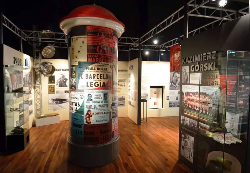 Sala ekspozycyjna Muzeum Legii Warszawa z kolumną obklejoną historycznymi plakatami meczowymi