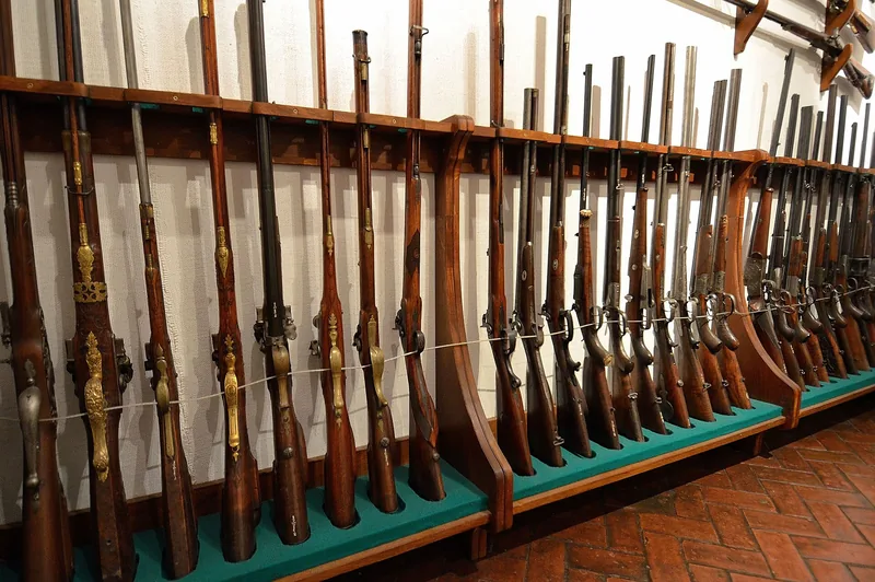 Długi rząd historycznej broni myśliwskiej ustawionej w drewnianych stojakach w Koszarach Kantonistów