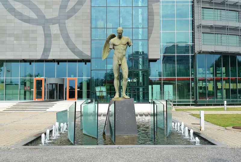 Brązowa rzeźba Ikaro Alato Igora Mitoraja w fontannie przed przeszklonym wejściem do Centrum Olimpijskiego
