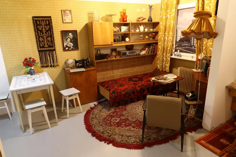 Odtworzony pokoj dzienny z epoki PRL - mebloscianka, dywan perski, fotel i lampa