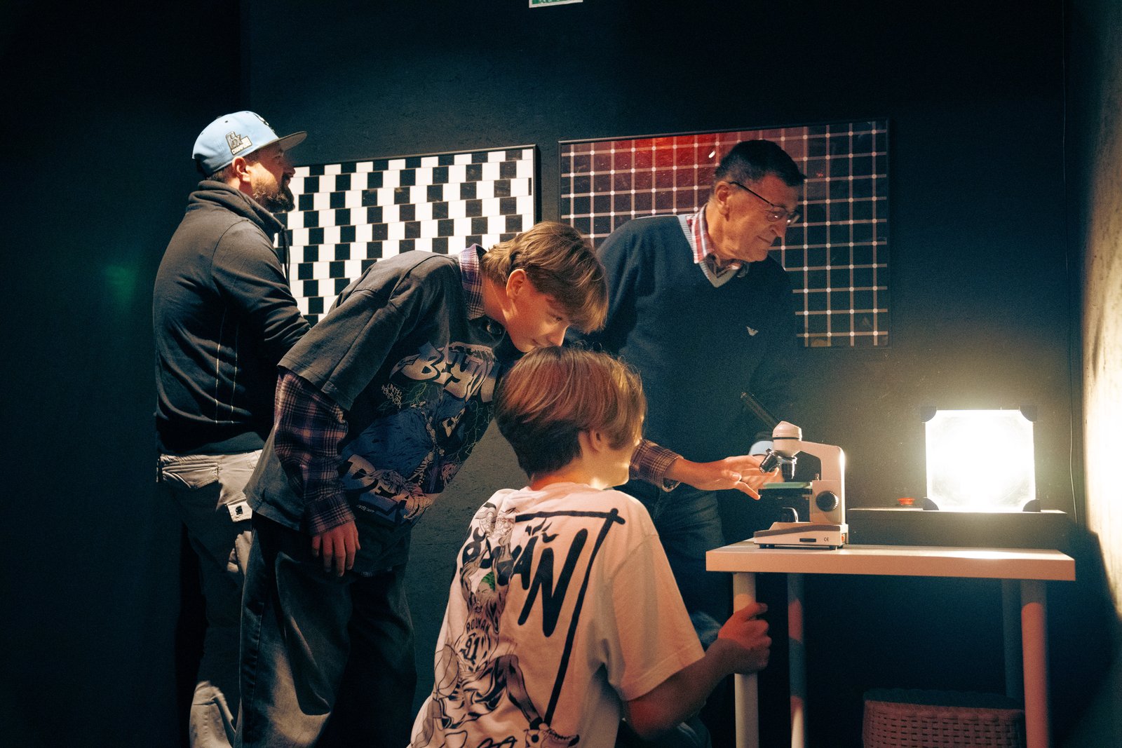 Visitors leaning over a microscope beside optical illusion panels at the WOMAI Science and Senses Centre in Krakow